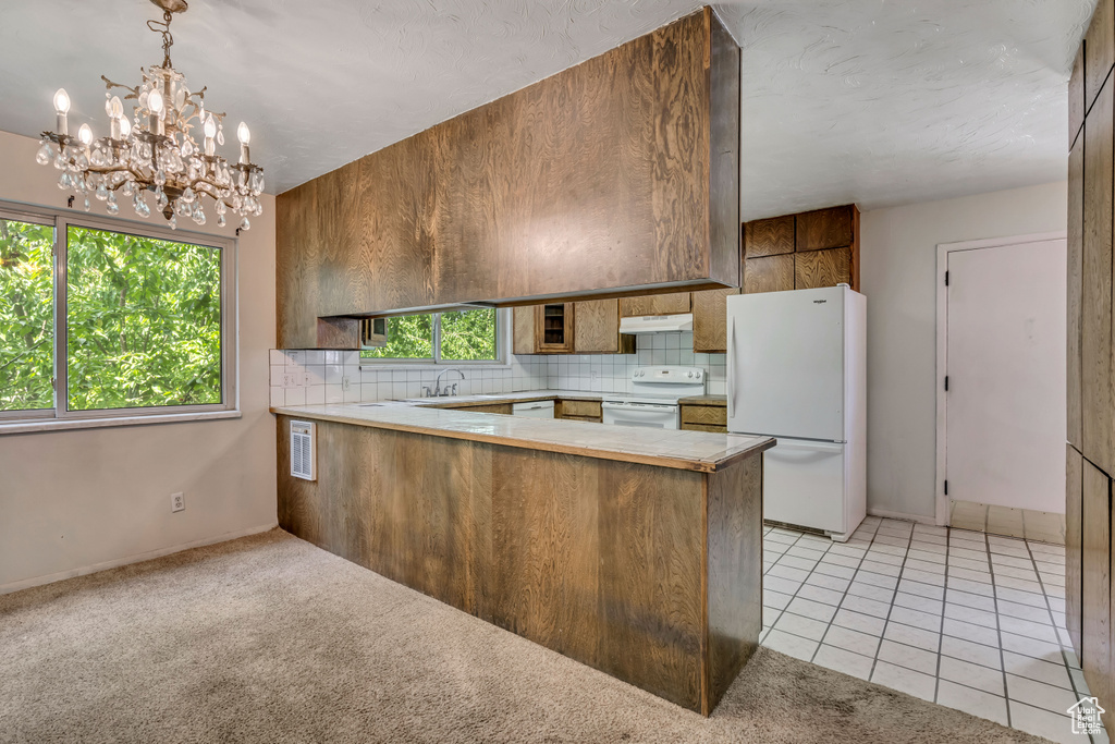 Kitchen featuring white appliances, under cabinet range hood, a peninsula, a chandelier, and light countertops