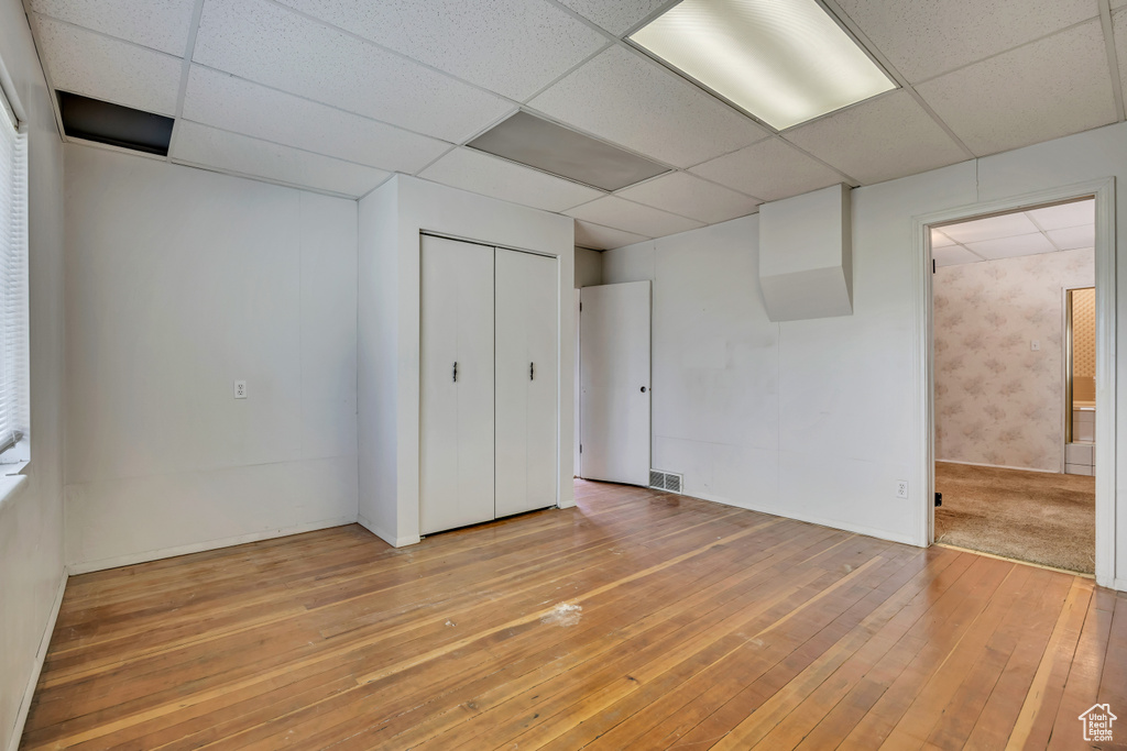 Unfurnished bedroom featuring a paneled ceiling, light wood-style flooring, connected bathroom, and a closet