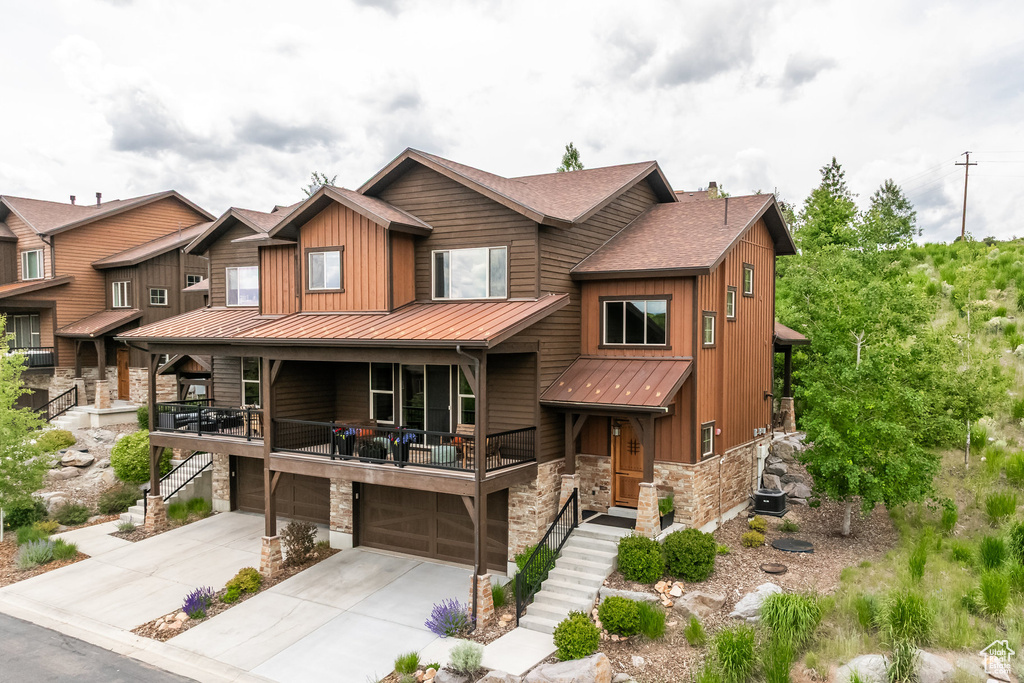 View of front of property featuring a standing seam roof, stone siding, stairs, an attached garage, and a metal roof
