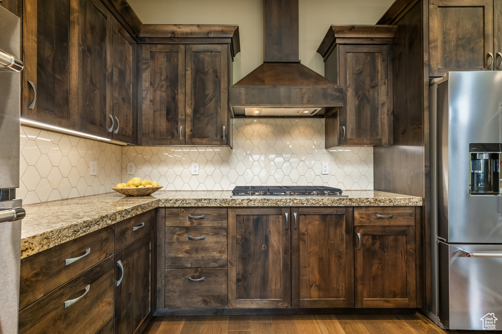 Kitchen with appliances with stainless steel finishes, wall chimney exhaust hood, dark brown cabinets, and tasteful backsplash