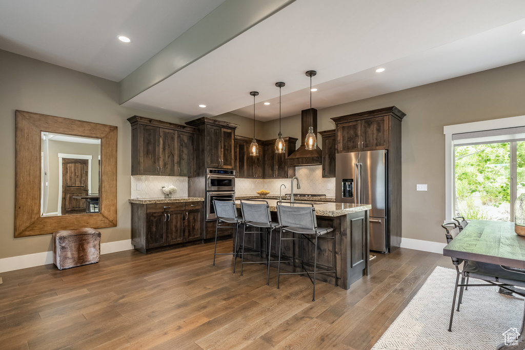 Kitchen featuring appliances with stainless steel finishes, dark brown cabinets, dark wood-style floors, a kitchen bar, and decorative backsplash