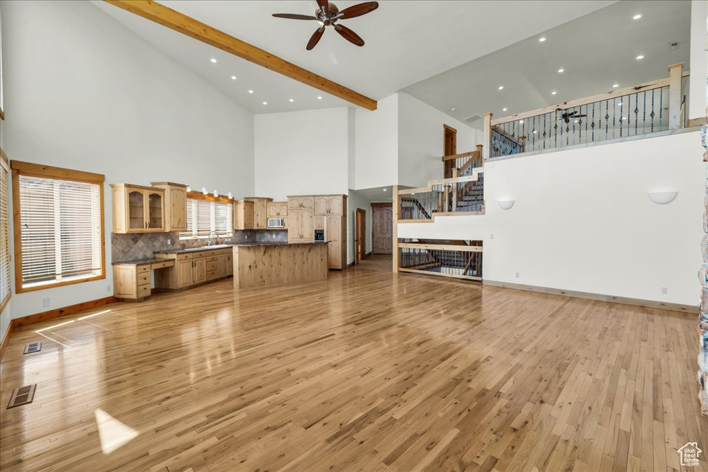 Unfurnished living room with a high ceiling, a ceiling fan, light wood-style floors, stairs, and recessed lighting