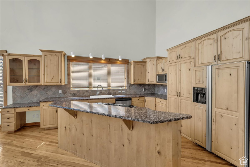 Kitchen with appliances with stainless steel finishes, light brown cabinets, a towering ceiling, a kitchen breakfast bar, and light wood-style floors