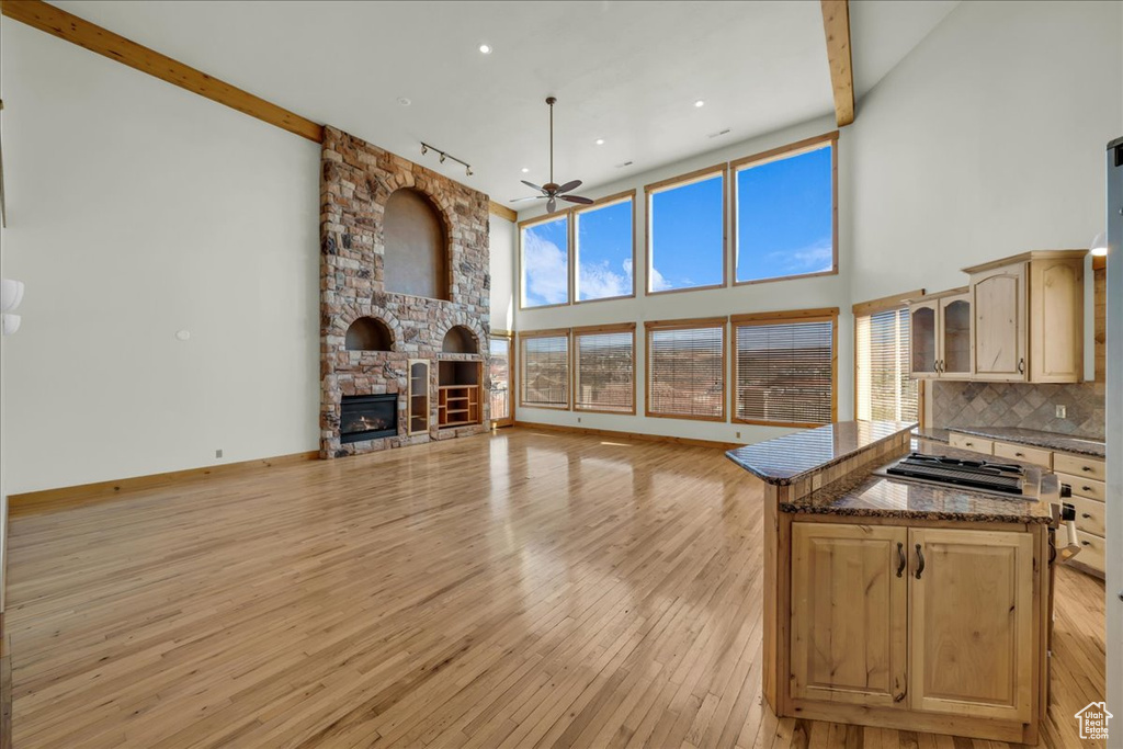 Living area featuring a ceiling fan, light wood-style flooring, a stone fireplace, a towering ceiling, and recessed lighting