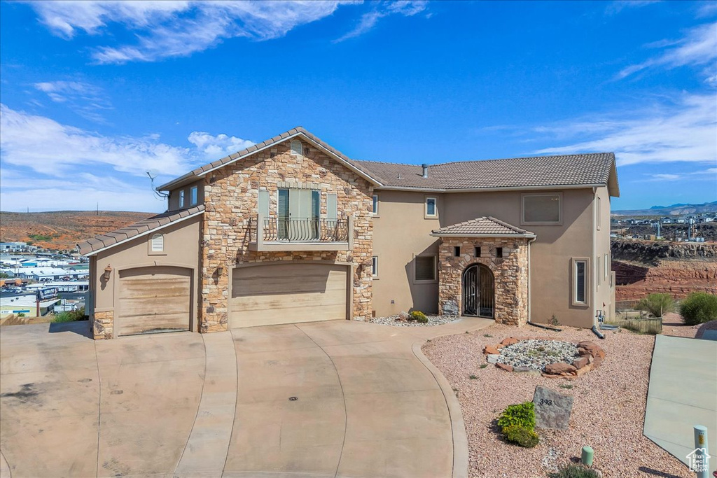 View of front of property with stone siding, stucco siding, a tile roof, concrete driveway, and a balcony
