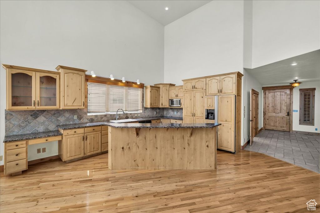 Kitchen featuring stainless steel microwave, high vaulted ceiling, light wood-style flooring, light brown cabinetry, and tasteful backsplash