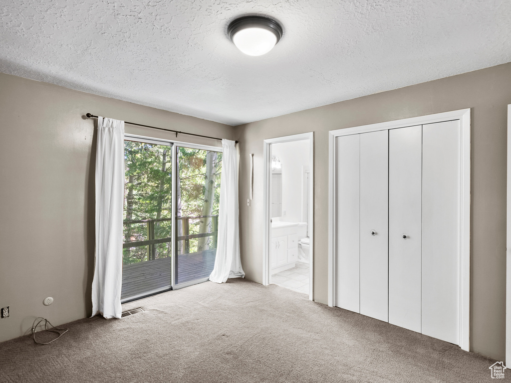 Unfurnished bedroom with carpet, access to exterior, a textured ceiling, connected bathroom, and a closet