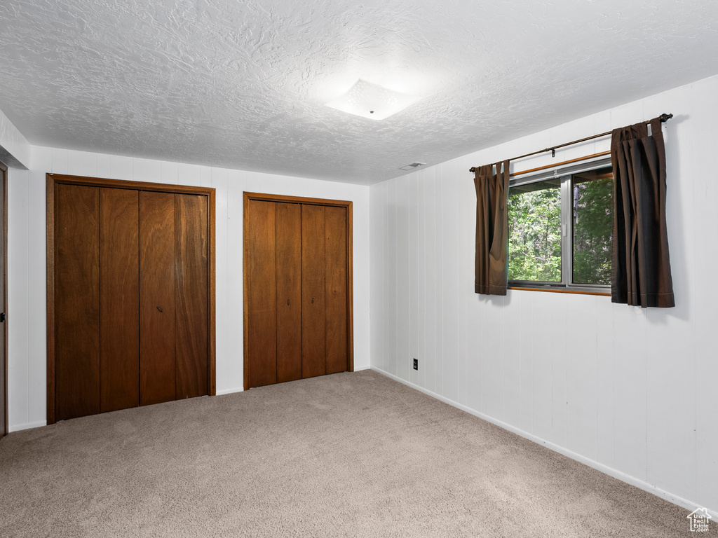 Unfurnished bedroom with a textured ceiling, multiple closets, and carpet flooring