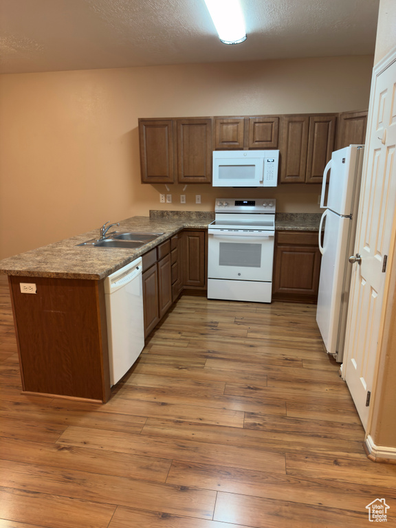 Kitchen with white appliances, a peninsula, light wood-type flooring, a textured ceiling, and brown cabinetry