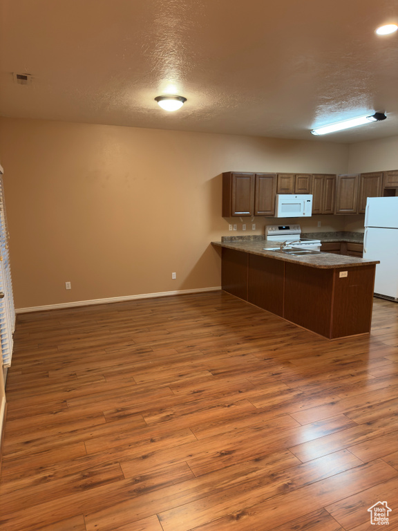 Kitchen featuring white appliances, a textured ceiling, a peninsula, wood finished floors, and open floor plan
