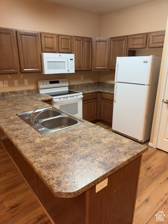 Kitchen featuring white appliances, a peninsula, light wood-style flooring, and brown cabinetry