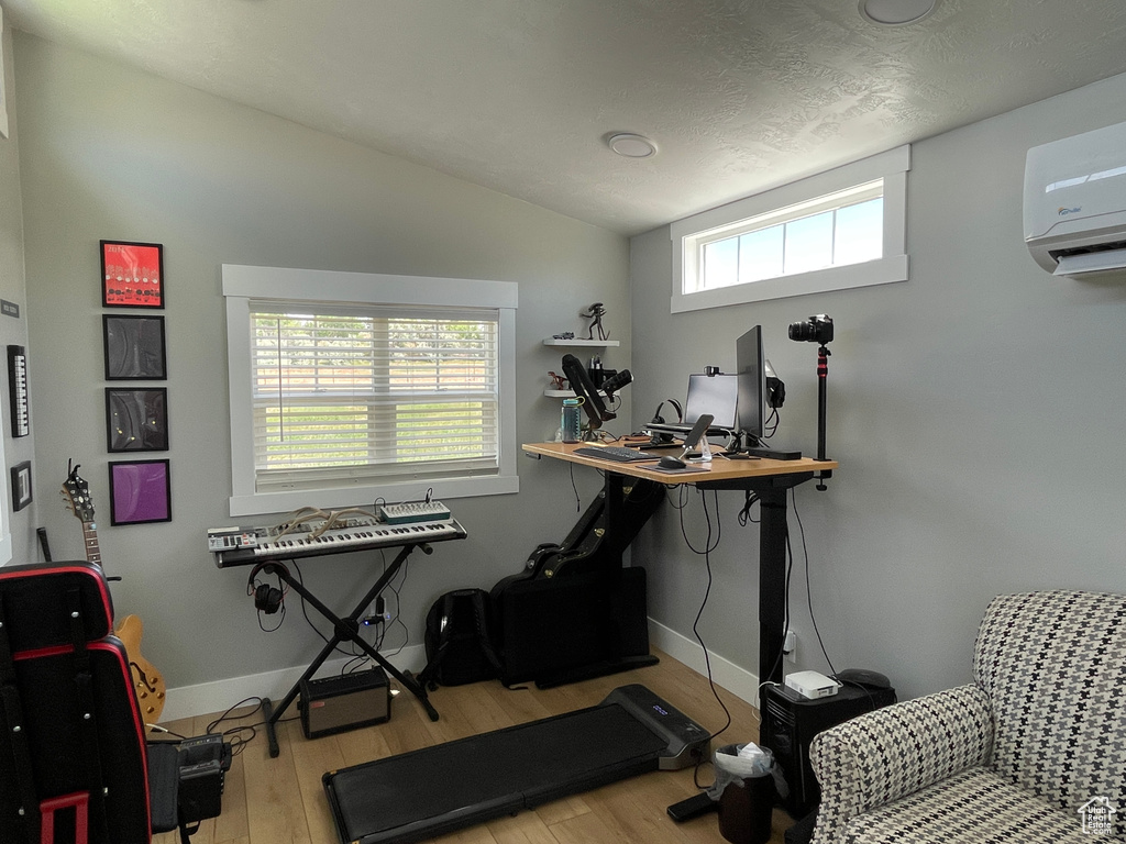 Home office with wood finished floors, lofted ceiling, and a wall mounted air conditioner