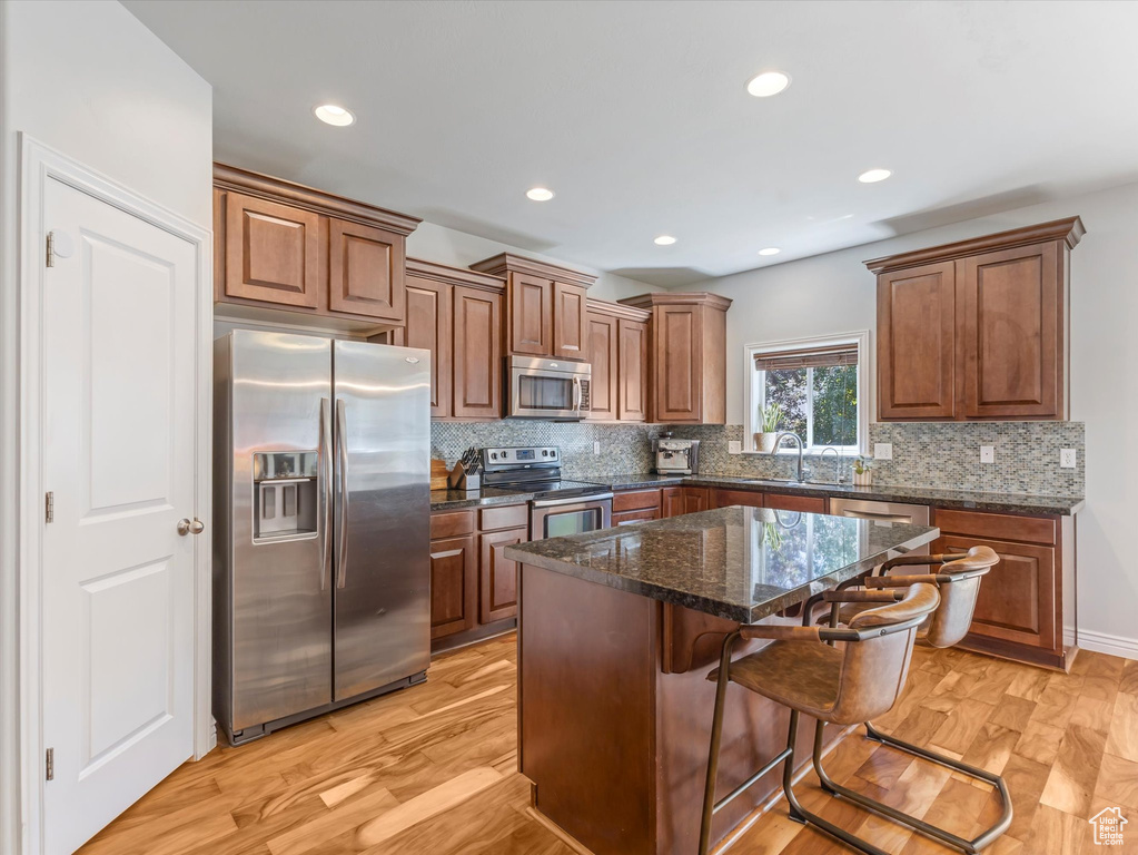 Kitchen featuring stainless steel appliances, backsplash, a kitchen breakfast bar, a kitchen island, and brown cabinetry
