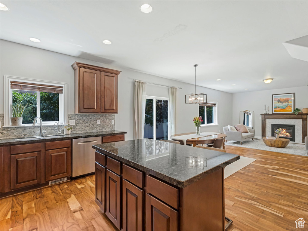 Kitchen featuring stainless steel dishwasher, backsplash, a center island, light wood-style flooring, and a glass covered fireplace