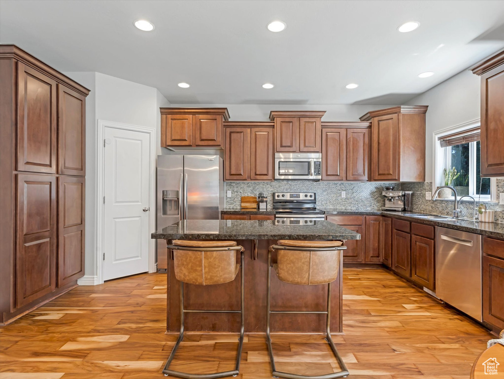 Kitchen featuring stainless steel appliances, a kitchen island, light wood-style floors, backsplash, and recessed lighting