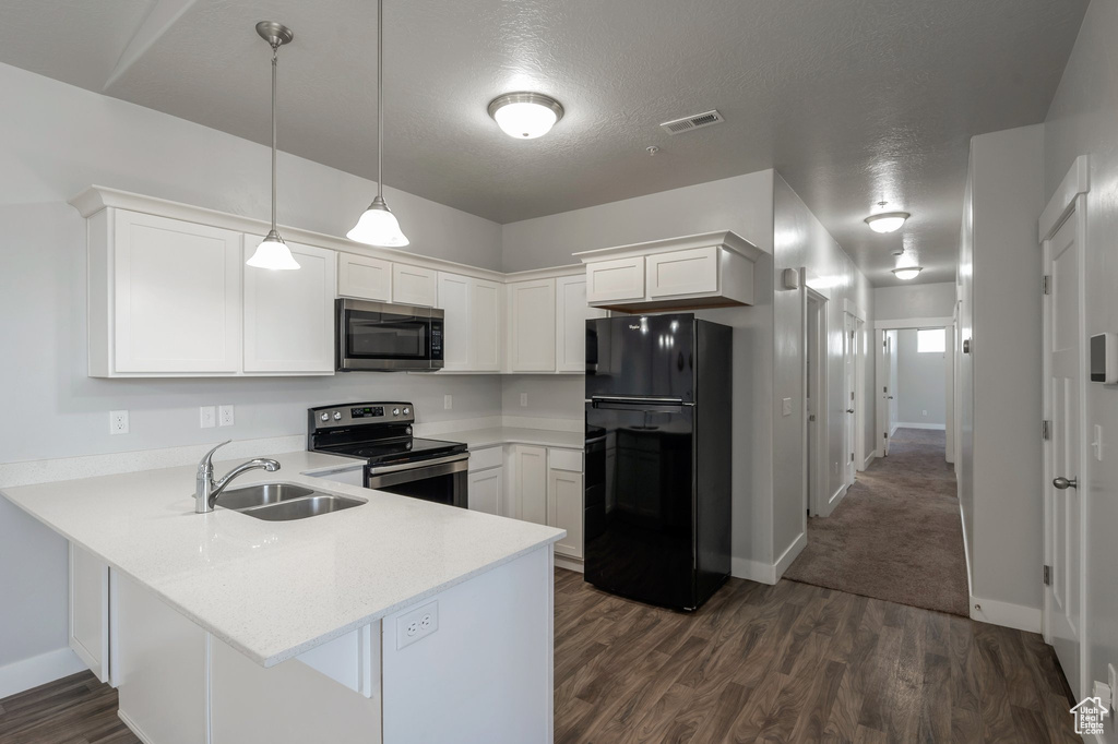 Kitchen with appliances with stainless steel finishes, a peninsula, white cabinets, dark wood-style floors, and hanging light fixtures