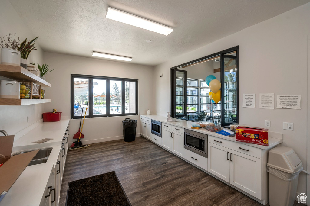 Kitchen featuring stainless steel microwave, dark wood-type flooring, white cabinets, open shelves, and a textured ceiling