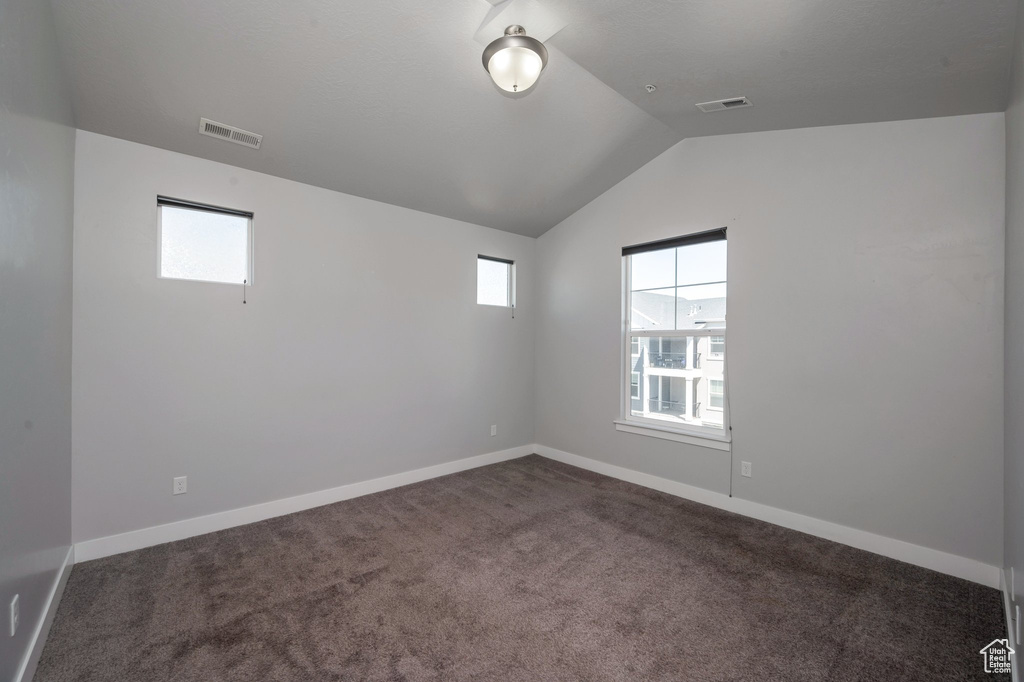 Spare room featuring vaulted ceiling and dark carpet