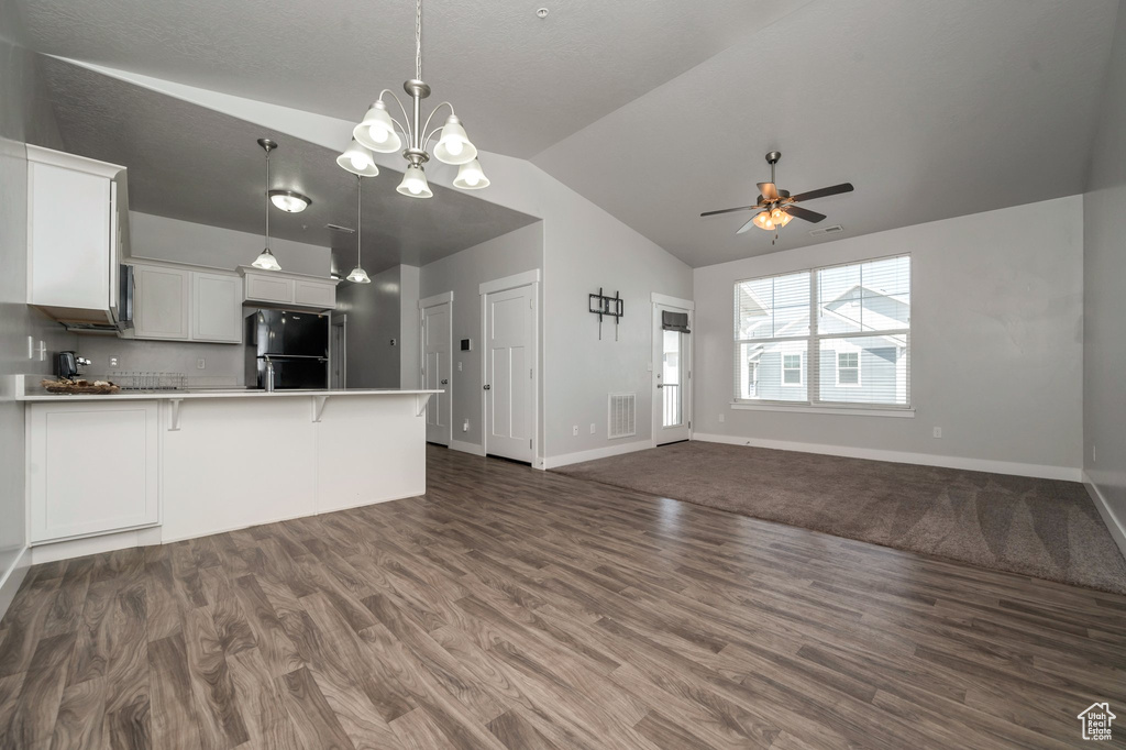 Kitchen with freestanding refrigerator, open floor plan, vaulted ceiling, a peninsula, and dark wood-type flooring