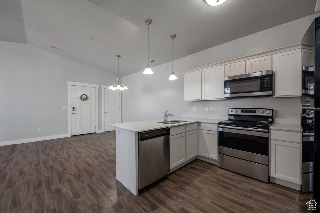 Kitchen with appliances with stainless steel finishes, vaulted ceiling, a peninsula, light countertops, and dark wood-style floors