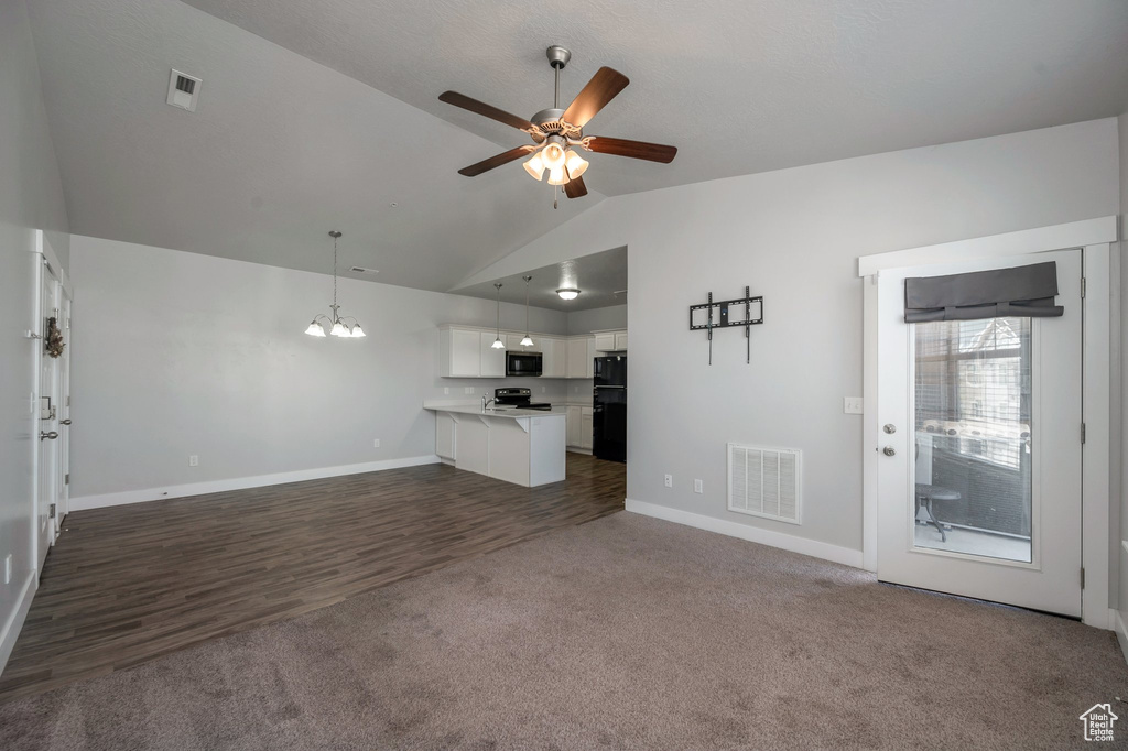 Unfurnished living room with lofted ceiling, ceiling fan, dark colored carpet, a chandelier, and dark wood-style floors