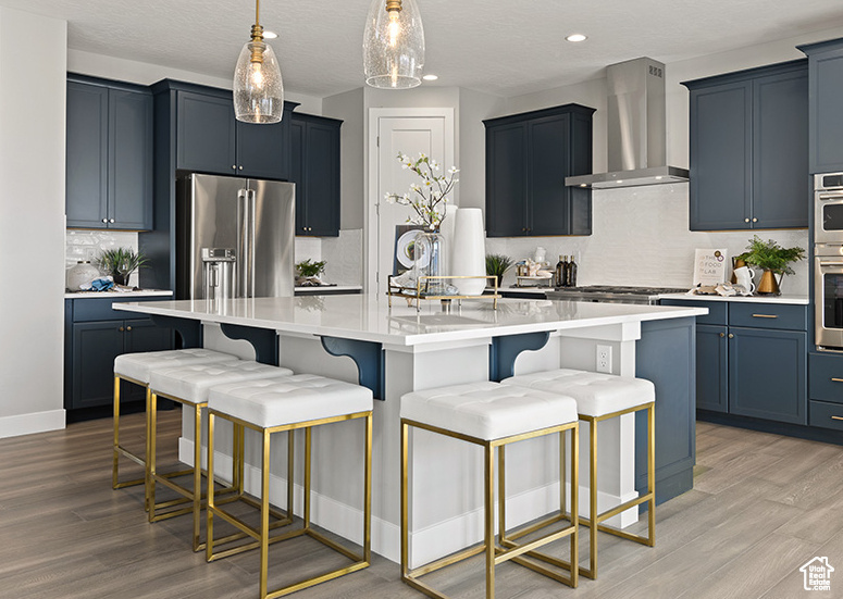 Kitchen with wall chimney range hood, light wood finished floors, stainless steel appliances, decorative backsplash, and recessed lighting