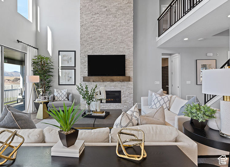 Living room featuring a high ceiling, a stone fireplace, healthy amount of natural light, and stairs