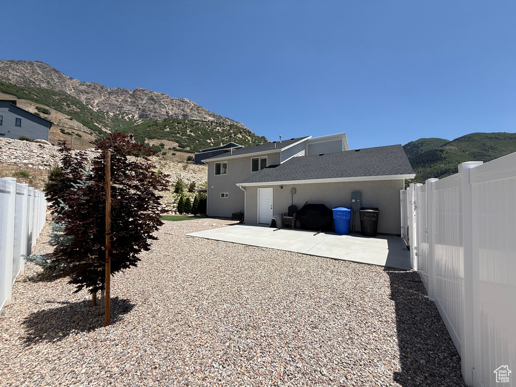 Rear view of house featuring a mountain view, a patio, and a shingled roof