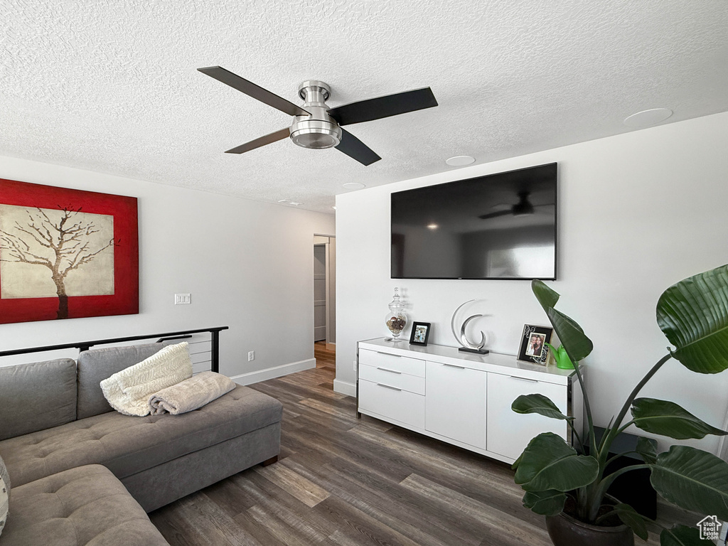 Living room featuring dark wood-type flooring, a ceiling fan, and a textured ceiling