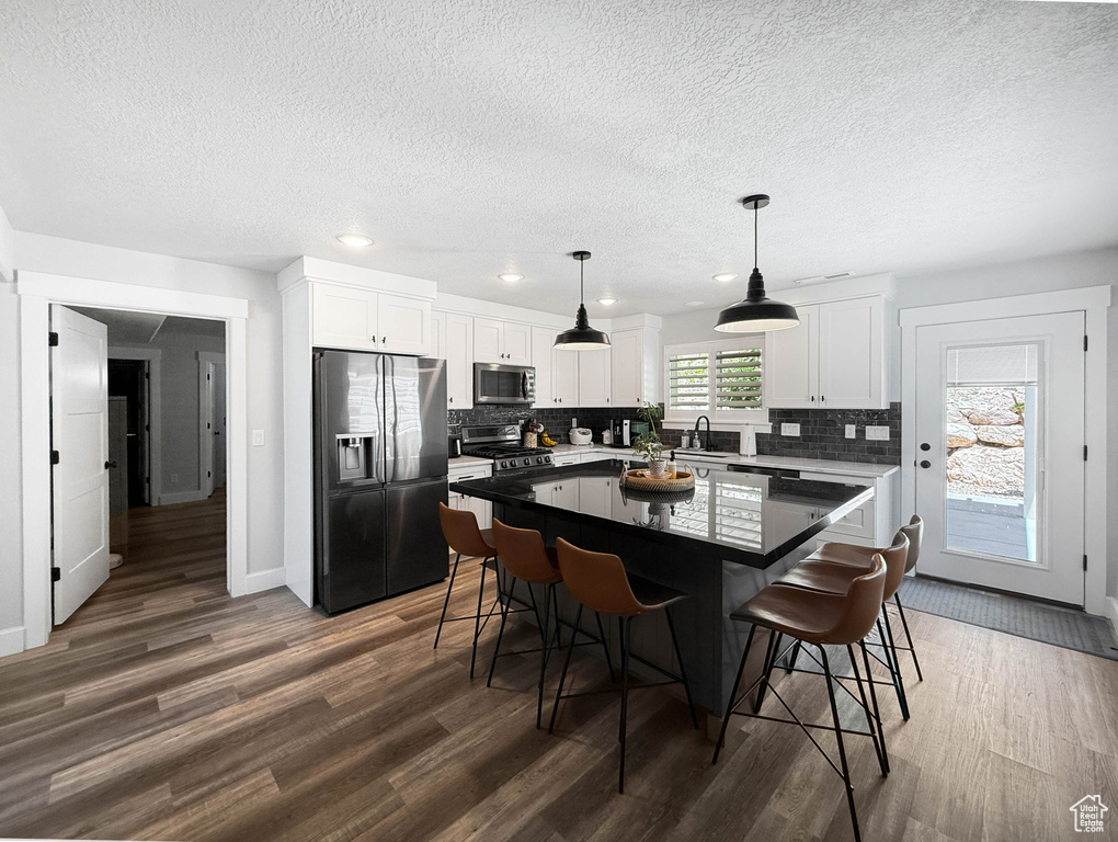 Kitchen featuring appliances with stainless steel finishes, a textured ceiling, dark wood-style floors, tasteful backsplash, and a breakfast bar