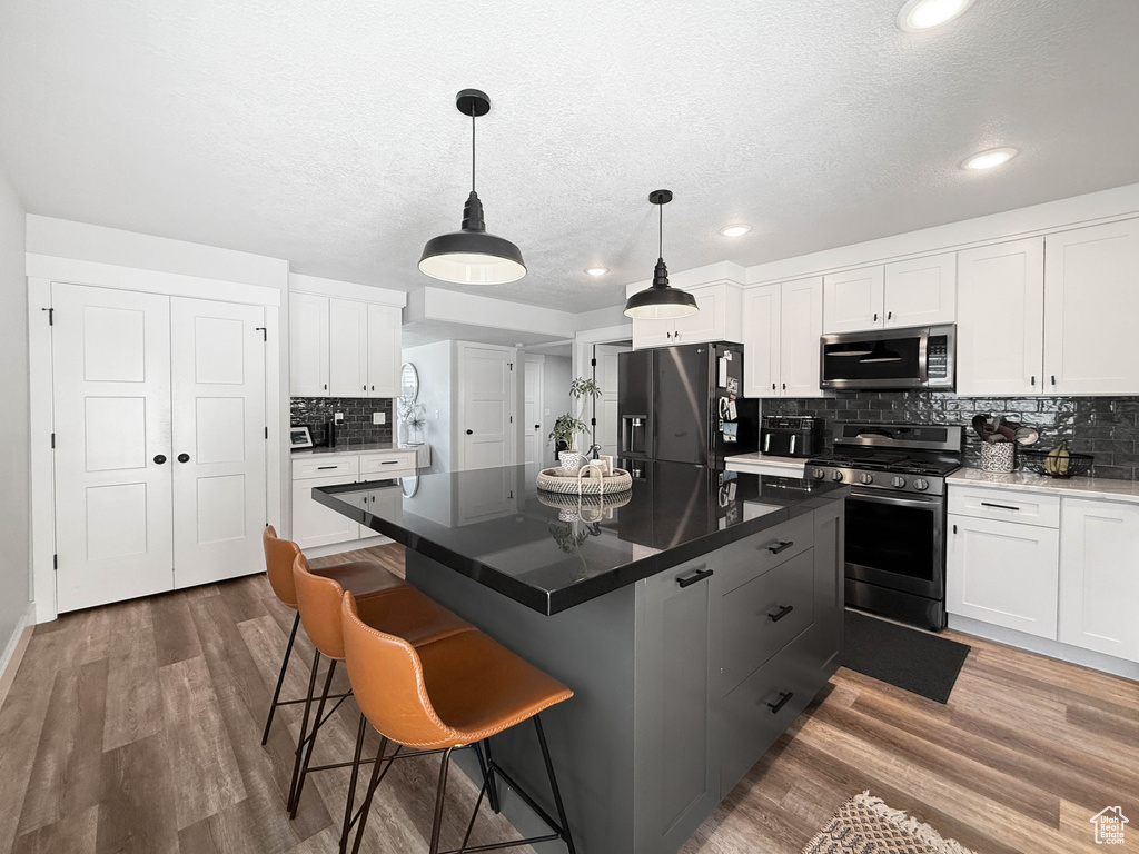 Kitchen featuring stainless steel appliances, tasteful backsplash, white cabinetry, a textured ceiling, and wood finished floors