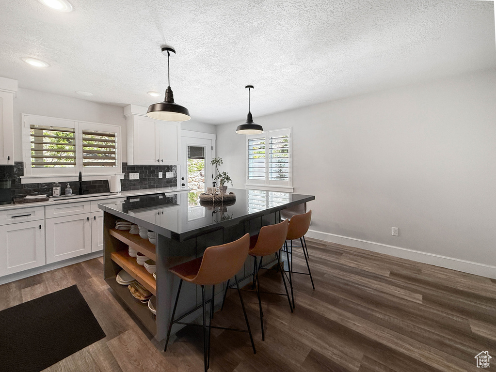 Kitchen featuring a kitchen bar, decorative backsplash, white cabinets, a textured ceiling, and recessed lighting