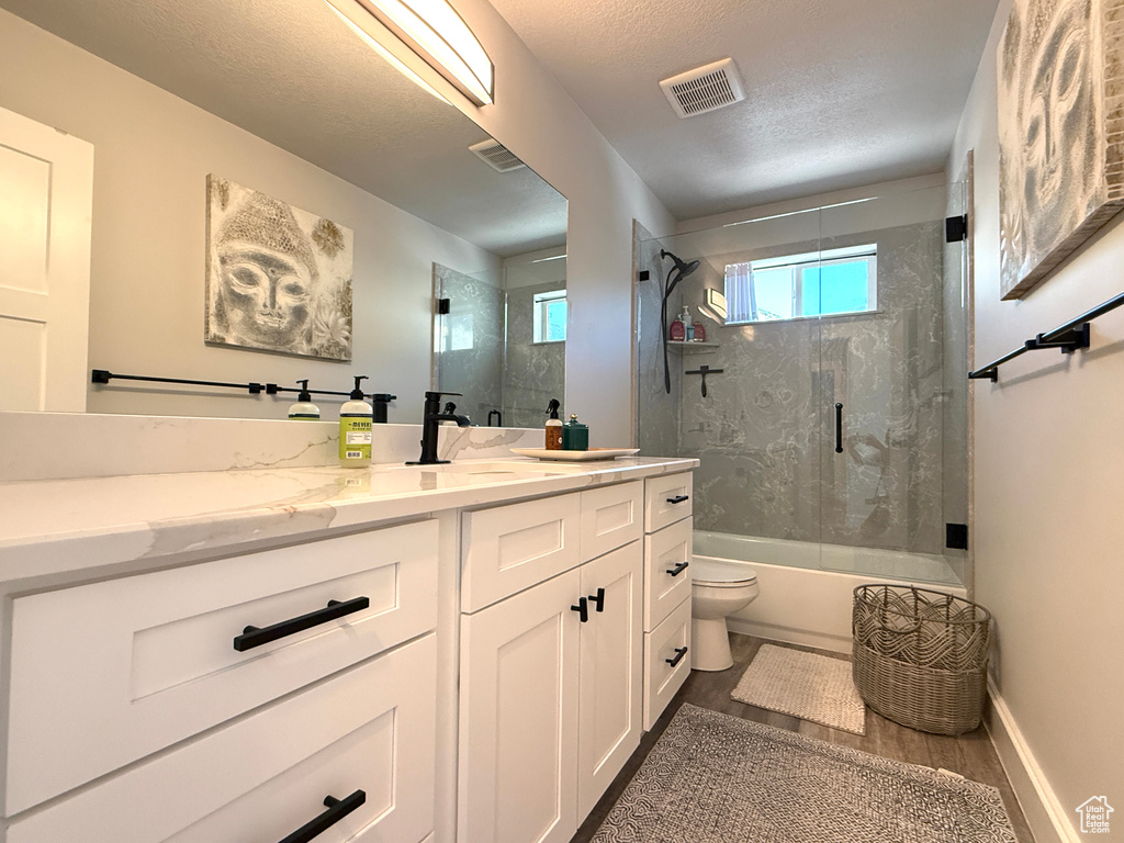 Bathroom with vanity, shower / bath combination with glass door, and a textured ceiling