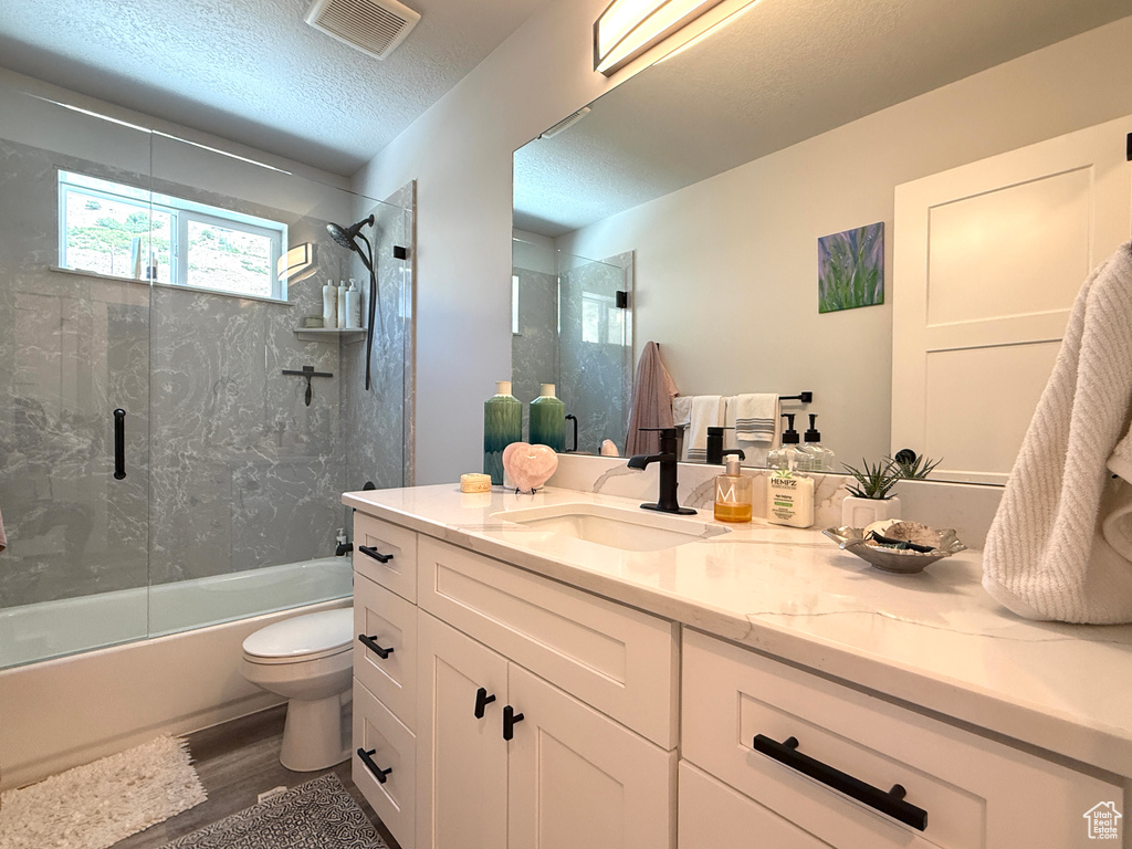 Full bath with vanity, combined bath / shower with glass door, wood finished floors, and a textured ceiling