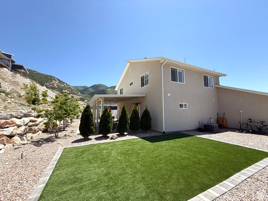 Rear view of property featuring stucco siding, a yard, a mountain view, and a patio