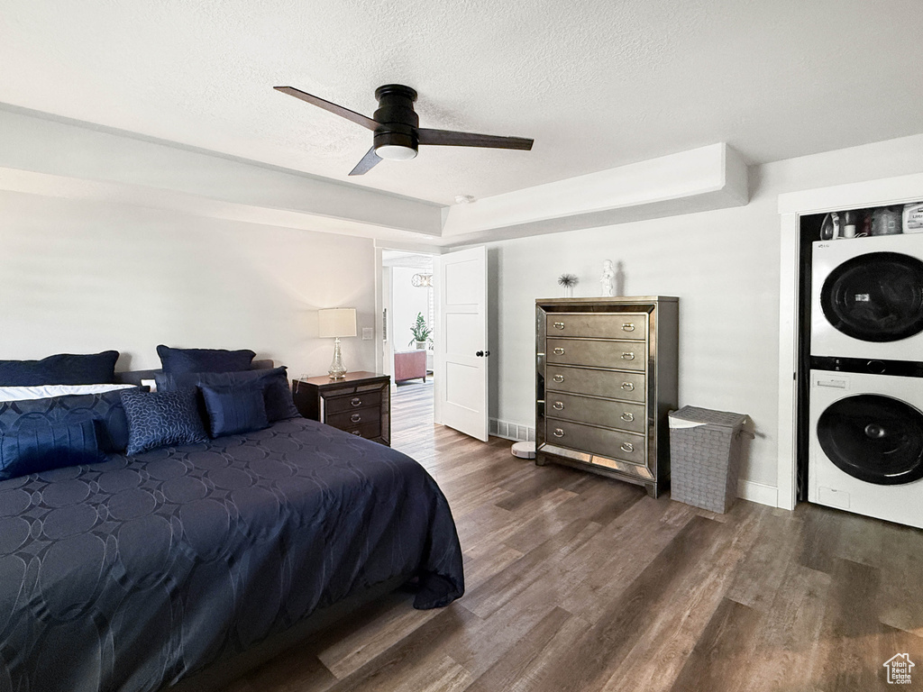 Bedroom featuring stacked washer / dryer, dark wood-style flooring, a textured ceiling, and ceiling fan