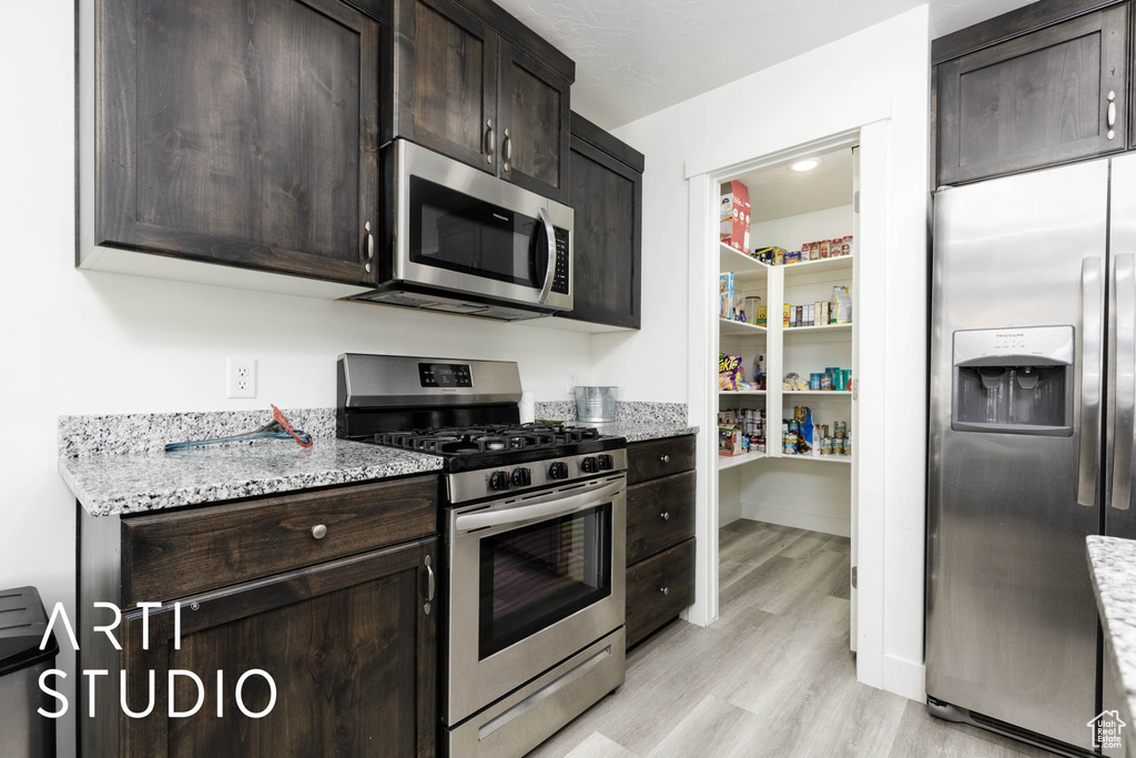 Kitchen with stainless steel appliances, light wood-style floors, dark brown cabinetry, and light stone counters