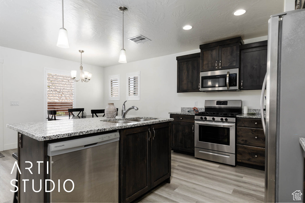 Kitchen featuring stainless steel appliances, light wood-style flooring, a chandelier, a center island with sink, and recessed lighting