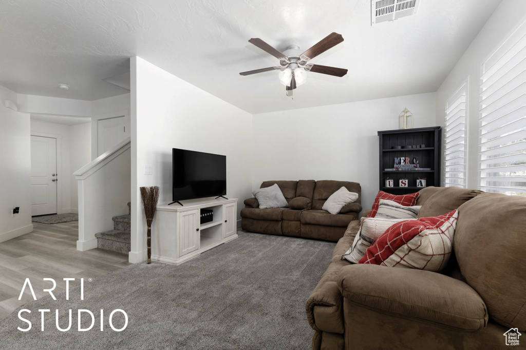 Living room with a ceiling fan, stairs, light carpet, and light wood finished floors