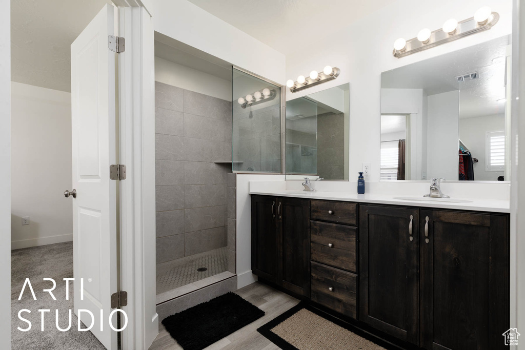 Bathroom featuring double vanity, a tile shower, and wood finished floors