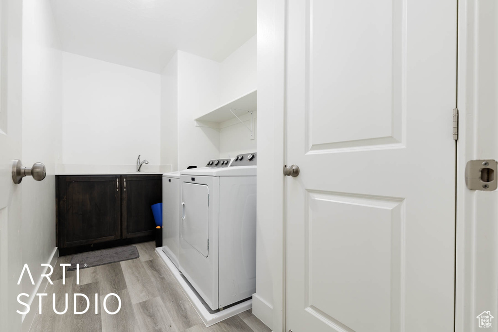 Laundry room with washer and dryer, light wood finished floors, and cabinet space