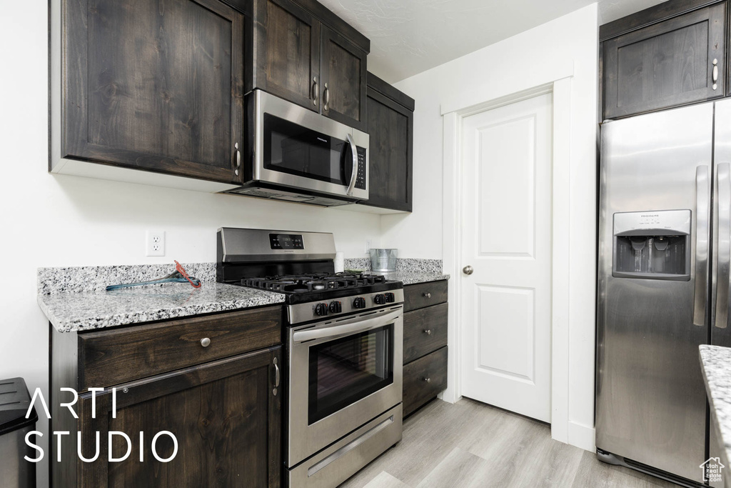 Kitchen featuring appliances with stainless steel finishes, light wood-style flooring, dark brown cabinetry, and light stone counters