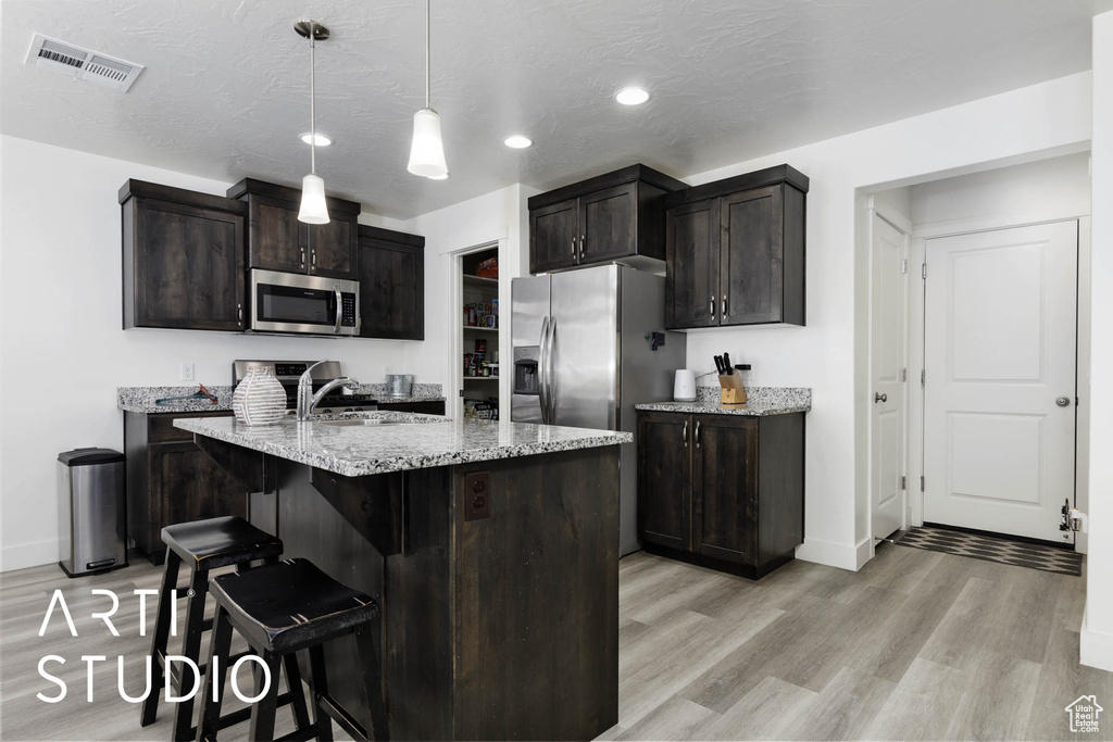 Kitchen with appliances with stainless steel finishes, light wood finished floors, light stone countertops, a breakfast bar area, and recessed lighting