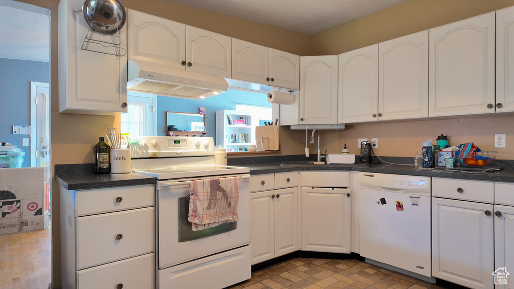 Kitchen with white appliances, under cabinet range hood, white cabinets, and dark countertops