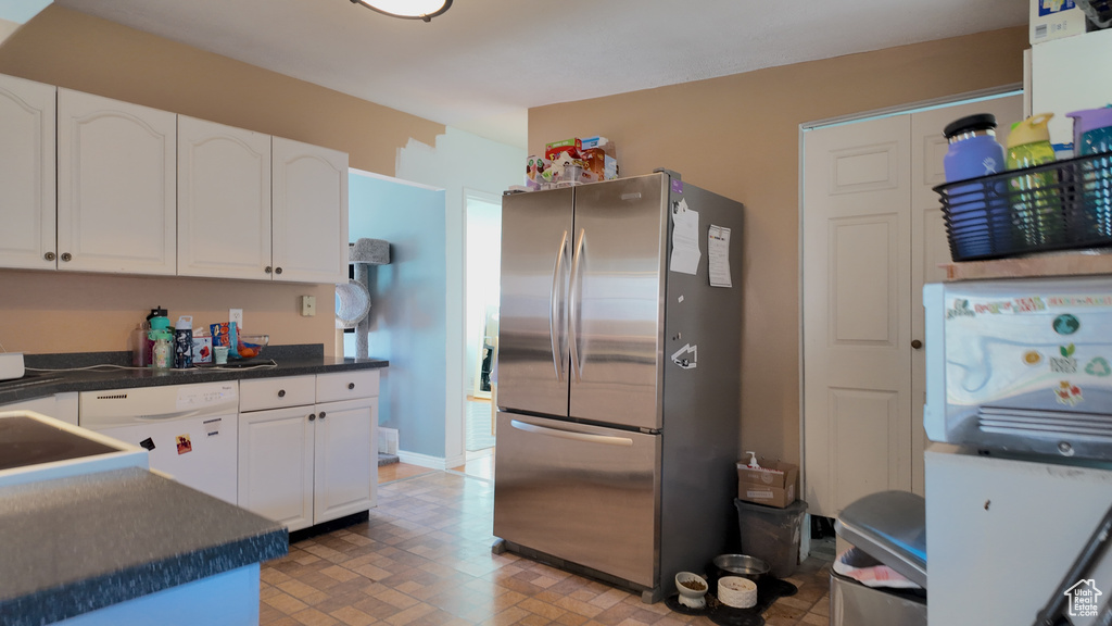 Kitchen with freestanding refrigerator, dishwasher, dark countertops, and white cabinetry