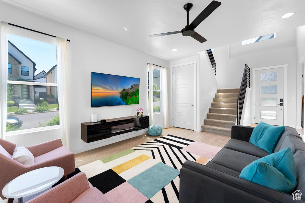 Living room featuring stairs, light wood-style flooring, ceiling fan, recessed lighting, and a skylight