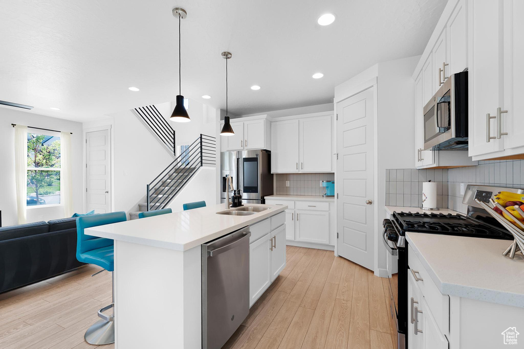 Kitchen with stainless steel appliances, light wood-style flooring, light countertops, decorative backsplash, and recessed lighting