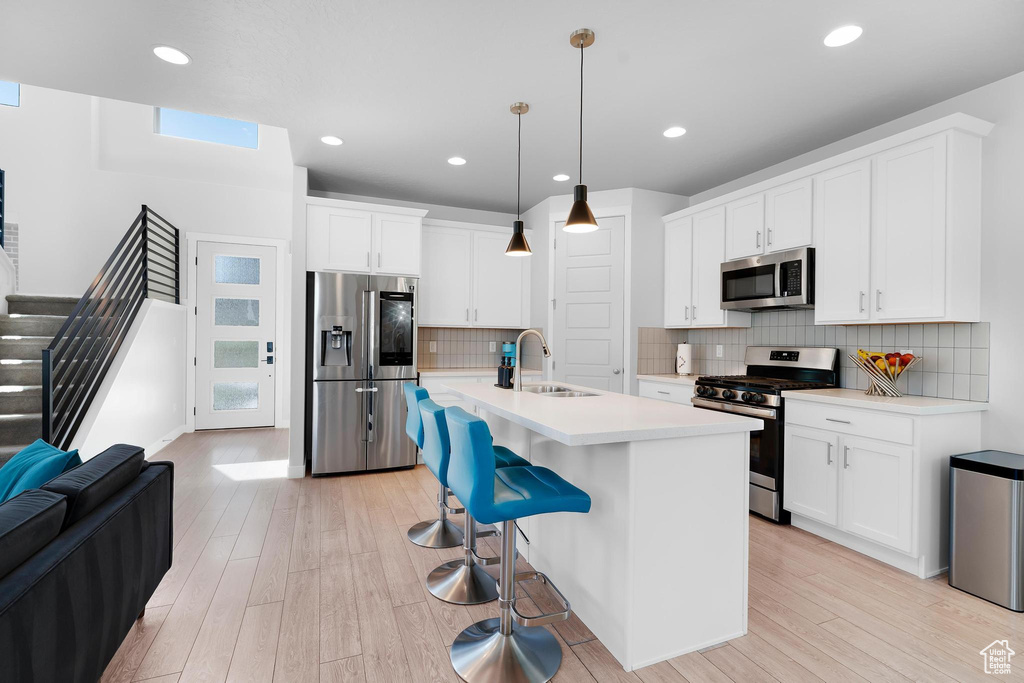 Kitchen featuring stainless steel appliances, light wood-style floors, light countertops, an island with sink, and white cabinetry