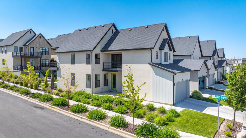 View of front of property featuring a residential view, a balcony, concrete driveway, a garage, and stucco siding