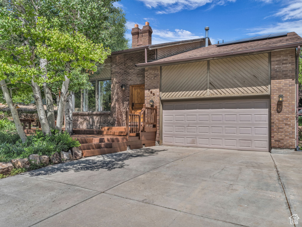 View of front of house with brick siding, driveway, a garage, and a chimney